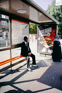 hombre, sentado, naranja, banco, junto a, mujer, en pie, edificio, estructura, parada de autobús, la carretera, ciudad, arquitectura, estructura construida, exterior del edificio, una persona, transporte, calle, modo de transporte, gente real, sendero, al aire libre, longitud total, vida en la ciudad, acera, comunicación, día, naturaleza, para caminar, esperando, 5K, CC0, dominio público, libre de derechos