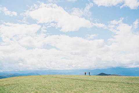 two, people, standing, grass field, blue, sky, white, clouds, daytime, green, grass, field, highland, mountain, man, woman, adventure, outdoor, camping, landscape, view, nature, beauty in nature, scenics, tranquility, tranquil scene, real people, day, cloud - sky, scenics - nature, environment, non-urban scene, land, leisure activity, men, plant, incidental people, idyllic, outdoors, 5K, CC0, public domain, royalty free