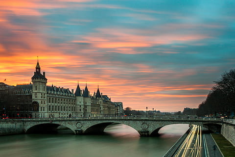 architecture, bridge, building, castle, city, conciergerie, dusk, light streaks, motion, outdoors, paris, river, sunset, time-lapse, water, built structure, bridge - man made structure, cloud - sky, sky, connection, building exterior, travel destinations, transportation, nature, tower, arch, arch bridge, no people, cityscape, government, 4K