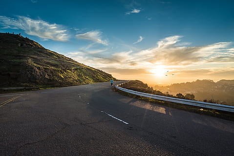 person, standing, beside, road guard rail, green, mountain, golden, hour, running, concrete, road, pavement, highway, sunset, sky, clouds, outdoors, landscape, nature, fitness, runner, people, guardrail, scenics, cloud - sky, transportation, no people, mode of transportation, direction, travel, the way forward, sunlight, sign, city, scenics - nature, sun, street, asphalt, dividing line, lens flare, multiple lane highway, 4K