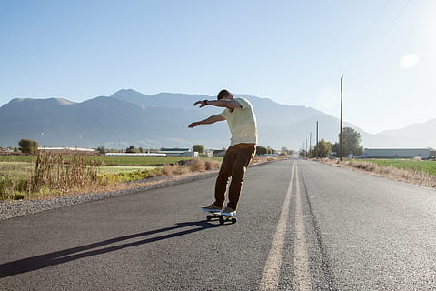 man skateboarding, road, people, man, guy, skateboard, sport, game, adventure, sunny, day, street, sky, one man only, adults only, one person, only men, casual clothing, leisure activity, adult, full length, one young man only, mountain, transportation, lifestyles, real people, sunlight, men, mountain range, nature, rear view, skill, clear sky, riding, human arm, diminishing perspective, outdoors, arms raised, 4K