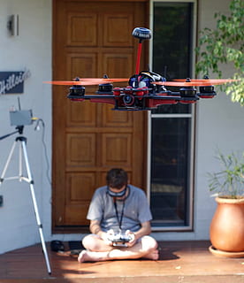 man, sitting, floor, beside, tripod, drone, quadcopter, control, stability, flight, flying, remote, first person view, quadrocopter, rotor, robot, one person, real people, lifestyles, front view, technology, table, lighting equipment, men, leisure activity, day, concentration, indoors, adult, waist up, photography themes, electric lamp, focus on foreground, occupation, 2K, CC0, public domain, royalty free