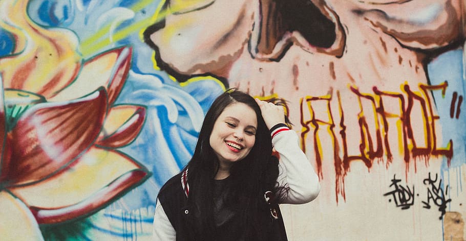dona, portar, negre, blanc, jaqueta de paperman, de peu, frontal, pintura mural, jaqueta de varsity, paret, graffiti, perforació, alternativa, hipster, femella, dones, gent, femelles, una persona, adult jove, a l'aire lliure, bonic, adult, una sola dona, només dones, multicolor, només adults, creativitat, art i artesania, funció de construcció de parets, art de carrer, arquitectura, cintura cap amunt, cabell, dones joves, vista frontal, roba, retrat, somrient, pentinat, cabell llarg, mural, dona guapa, 5K