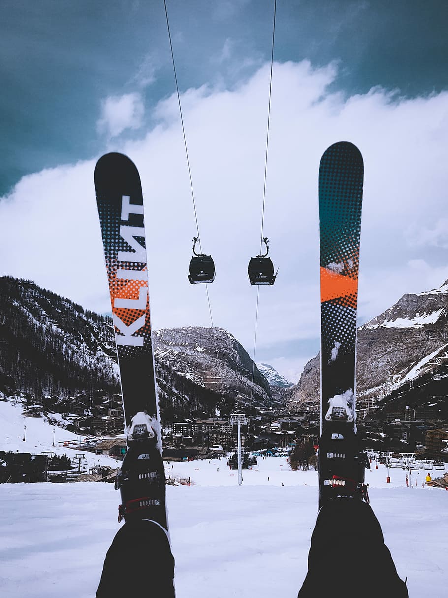 person, sidder, sne, iført, sne skis, grøn-og-orange sne ski, ski, skilift, bjerg, skyer, skiløber, vinter, kold temperatur, himmel, natur, sky - himmel, skønhed i naturen, transportmidler, rigtige mennesker, fritidsaktivitet, flag, dag, bjergkæde, scenics - natur, svævebane, livsstil, sport, miljø, udendørs, snedækket bjerg, 4K