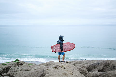 persona in possesso di tavola da surf, persona, detenzione, rosso, tavola da surf, riva del mare, uomo, blu, felpa con cappuccio, giacca, Marrone, massi, bianca, skimboard, corpo d'acqua, giorno, Surf, costa, nube, oceano, acqua, spiaggia, mare, all'aperto, natura, una persona, persone, estate, donne, divertimento, cielo, vacanze, solo adulti, adulto, orizzonte sull'acqua, adulto maturo, terra, bellezza nella natura, lunghezza intera, roccia, roccia - oggetto, retrovisore, solitudine, solido, attività di svago, in piedi, scenics - natura, guardando a vista, 5K, CC0, dominio pubblico, privo di copyright