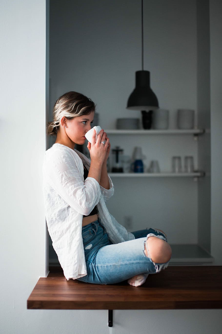 kvinne, nipper, kopp, hvit, sitter, vindu, brun, tre, plattform, keramisk, én person, innendørs, uformelt antrekk, holding, full lengde, sidevisning, voksen, ung voksen, jeans, sete, hjem interiør, kvinner, dag, avslapning, fritidsaktivitet, hjemlige rom, tre kvart lengde, drikkevann, frisyre, uskyld, tanke, 5K