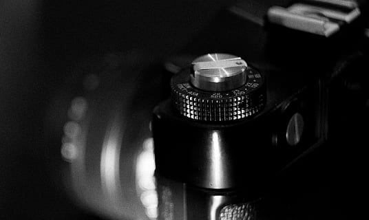 black-and-white, camera, close-up, equipment, camera - Photographic Equipment, technology, indoors, photography themes, focus on foreground, no people, lens - optical instrument, photographic equipment, arts culture and entertainment, lens - eye, single object, slr camera, camera film, selective focus, still life, retro styled, digital camera, black background, 2K, CC0, public domain, royalty free