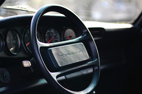 Porsche 1987, Nahansicht, Foto, schwarz, Porsche Lenkrad, Auto, Rad, Innere, Innerhalb, Design, Transportmittel, Transport, Kraftfahrzeug, Fahrzeuginnenraum, Landfahrzeug, Autoinnenraum, Lenkrad, Schalttafel, keine Leute, Instrumententafel, Technologie, Glas - Material, drinnen, Rückspiegel, Reflexion, Reise, Fokus auf den Vordergrund, Luxus, Fahrzeugspiegel, 5K, CC0, gemeinfrei, lizenzfrei