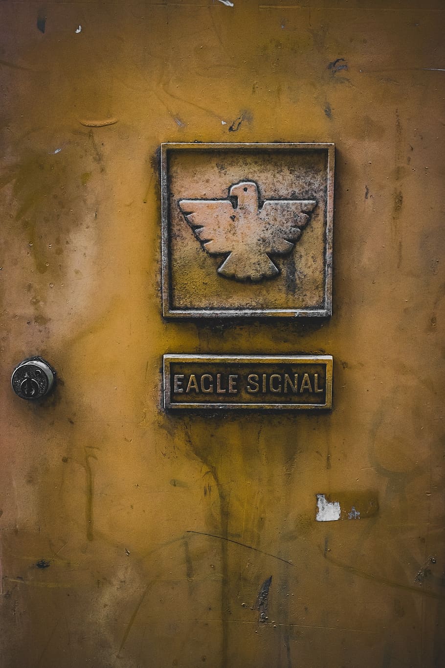 Adler-Signal-Emblem, Adler-Signal-Logo, Zeichen, Tür, sperren, Adler, Signal, Text, Kommunikation, westliche Schrift, keine Leute, Wandbau - Funktion, alt, die Architektur, gebaute Struktur, Nahansicht, Großbuchstabe, Metall, Tag, Kunst und Handwerk, Gelb, verwittert, drinnen, Darstellung, Wand, Kreativität, 5K