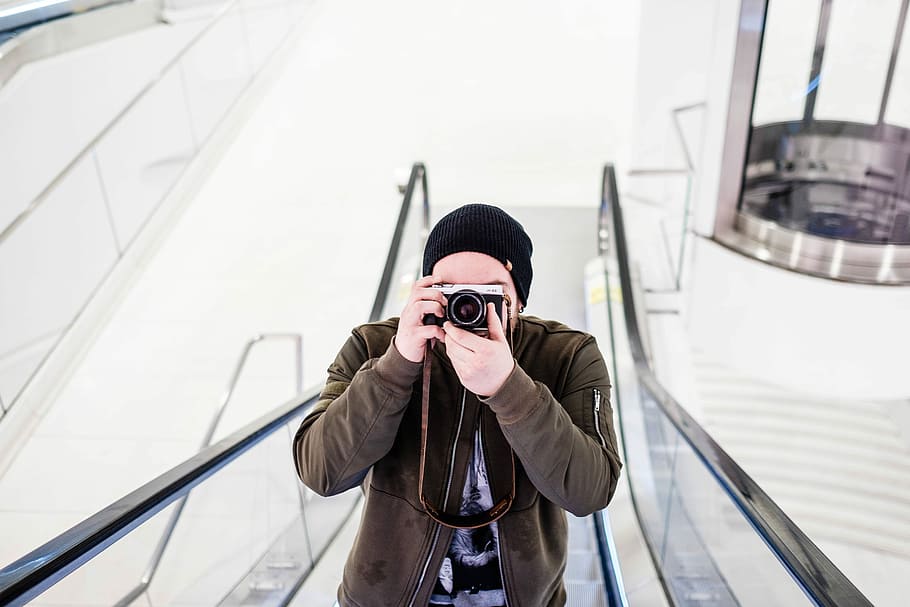 mężczyzna, trzymać, ruchome schody, slr camera, na dworze, mężczyźni, ludzie, jedna osoba, dorosły, kaukaskie pochodzenie etniczne, aparat fotograficzny - sprzęt fotograficzny, podróżować, przedni widok, tylko dla dorosłych, tylko jeden człowiek, tematy fotograficzne, fotografowanie, technologia, prawdziwi ludzie, sprzęt fotograficzny, transport, styl życia, dzień, czynność, spędzania wolnego czasu, architektura, kurtka, na stojąco, codzienne ubrania, fotograf, aparat cyfrowy, zasłonięta twarz, ciepłe ubranie, 5K