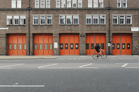 home, muntar a cavall, bicicleta, marró, edifici, durant el dia, arquitectura, infraestructura, estructura, establiment, apartament, finestres, condomini, hotel, gent, cicle, casc, carretera, carrer, escena urbana, a l'aire lliure, transport, estructura construïda, exterior de l'edifici, manera de transport, ciutat, vehicle terrestre, marcatge, marcatge de carreteres, persones reals, símbol, signe, dia, finestra, una persona, 4K, CC0, domini públic, lliure de regalies