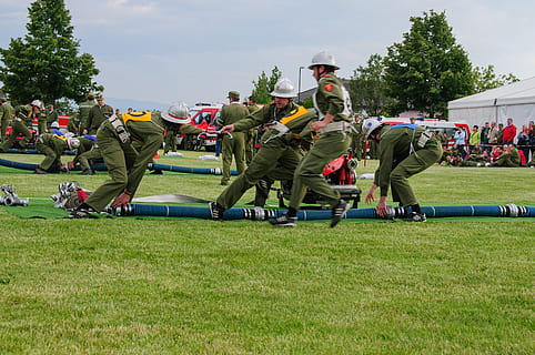 Fire, Competition, Competitions, fire fighting attack, firefighter competition, grass, sport, playing field, field, large group of people, plant, group of people, real people, men, crowd, clothing, nature, day, tree, green color, uniform, teamwork, cooperation, sky, outdoors, event, marching band, spectator, government, 2K, CC0, public domain, royalty free