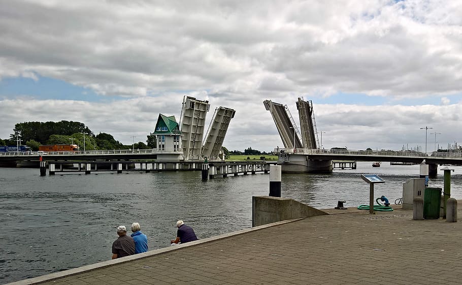 tres, persona, assegut, cos, aigua, pont, pont basculant, edifici, construcció, pont de carretera, apareix, schlei, fiord del mar bàltic, kappeln, Alemanya del nord, arquitectura, estructura construïda, cel, riu, núvol - cel, exterior de l'edifici, connexió, pont - estructura feta per l'home, ciutat, transport, naturalesa, destinacions de viatge, homes, adult, dues persones, gent, 2K