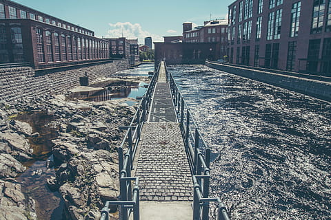 black, metal bridge, middle, water, metal, bridge, near, buildings, architecture, structures, walkways, paths, industrial, dirty, rocks, sewage, city, urban, metro, railroad track, rail transportation, no people, transportation, outdoors, day, built structure, building exterior, sky, nature, track, the way forward, direction, railing, building, diminishing perspective, connection, surface level, 4K