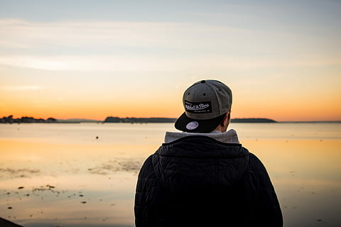 Mann, iført, lokk, stående, vendt, kropp, vann, svart, jakke, grå, flat-surf cap, hatt, fyr, bak, soloppgang, solnedgang, frakk, hette, sand, hav, horisont, oransje, himmel, utsikt bakover, ekte folk, én person, land, natur, skjønnhet i naturen, livsstil, fritidsaktivitet, Strand, naturskjønnhet - natur, fra livet opp, menn, varme klær, 5K, CC0, offentlig domene, opphavsrett gratis
