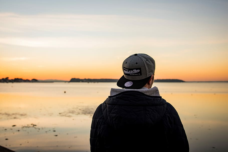 Mann, iført, lokk, stående, vendt, kropp, vann, svart, jakke, grå, flat-surf cap, hatt, fyr, bak, soloppgang, solnedgang, frakk, hette, sand, hav, horisont, oransje, himmel, utsikt bakover, ekte folk, én person, land, natur, skjønnhet i naturen, livsstil, fritidsaktivitet, Strand, naturskjønnhet - natur, fra livet opp, menn, varme klær, 5K