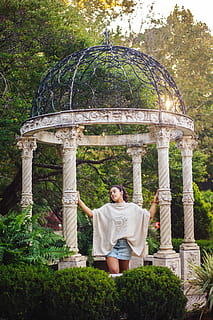 fotografia, donna, detenzione, post gazebo, in piedi, gazebo, struttura, architettura, pavillion, colonna, pilastro, una persona, pianta, natura, persone reali, albero, attività di svago, abbigliamento casual, stili di vita, vista frontale, giorno, adulto, ritratto, crescita, lunghezza intera, giardino, sorridente, metà adulto, all'aperto, 5K, CC0, dominio pubblico, privo di copyright