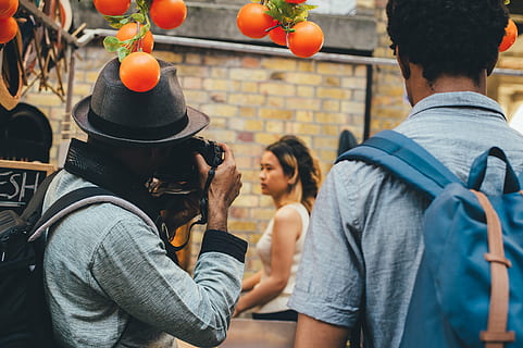 adult, backpack, blur, camera, city, daylight, focus, group, hat, man, outdoors, people, street, urban, wear, woman, men, real people, lifestyles, casual clothing, young men, young adult, leisure activity, group of people, friendship, women, holding, rear view, togetherness, architecture, day, technology, communication, focus on foreground, jeans, 4K