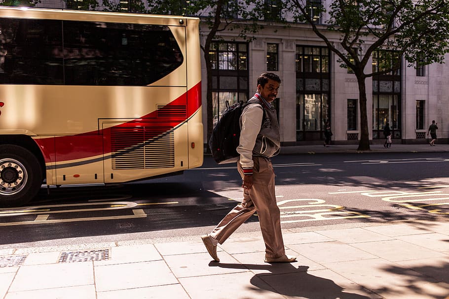 uomo, a piedi, marciapiede, in piedi, autobus, strada, allenatore, fotografia di strada, uomo che cammina, urbano, albero, ombra, zaino in spalla, zaino, costruzione, città, latino, lunghezza intera, una persona, mezzi di trasporto, modo di trasporto, architettura, abbigliamento casual, giovane adulto, giorno, adulto, stili di vita, luce del sole, auto, veicolo a motore, giovani uomini, esterno dell'edificio, all'aperto, 5K
