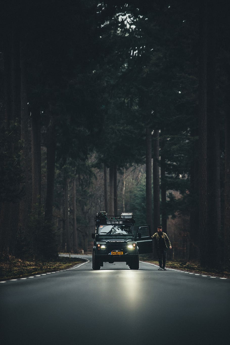 home, marró, jaqueta, de peu, al costat, cotxe, carretera, caminar, land rover suv, alt, arbres, bosc, arbre, llum, transport, manera de transport, planta, vehicle terrestre, naturalesa, persones reals, automòbil, viatjar, creixement, terra, el camí a seguir, homes, dia, a l'aire lliure, tronc de l'arbre, direcció, viatge de carretera, 5K