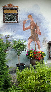 Fassade, Wand, Wandgemälde, bemalte Wand, Garten, Bayern, bunt, Künstler, Pflanze, blühende Pflanze, Blume, die Architektur, Gebäudehülle, Natur, gebaute Struktur, Tag, Religion, Spiritualität, Kunst und Handwerk, Topfpflanze, Gebäude, menschliche Darstellung, Glauben, Rückansicht, draußen, Darstellung, eine Person, Skulptur, menschlicher Arm, Arme erhoben, Blumenschmuck, 4K, CC0, gemeinfrei, lizenzfrei