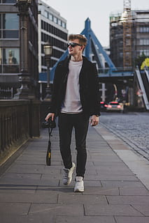superficiale, fotografia a fuoco, uomo, detenzione, fotocamera dslr, fotocamera nikon dslr, a piedi, lato, strada, strada cementata, nero, giacca, pantaloni, all'aperto, una persona, persone, etnia caucasica, giovane adulto, scena urbana, uomini, adulto, stili di vita, occhiali da sole, vita di città, città, abbigliamento casual, moda, sorridente, maschi, ritratto, solo un uomo, Solo uomini, lunghezza intera, vista frontale, in piedi, architettura, giovani uomini, bicchieri, esterno dell'edificio, persone reali, struttura costruita, giorno, attività di svago, 4K, CC0, dominio pubblico, privo di copyright