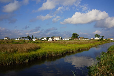 river, town, grass, marshland, clouds, reflection, buildings, rural, water, sky, cloud - sky, tranquility, scenics - nature, plant, tranquil scene, beauty in nature, landscape, nature, no people, architecture, green color, building, built structure, house, environment, outdoors, 2K, CC0, public domain, royalty free